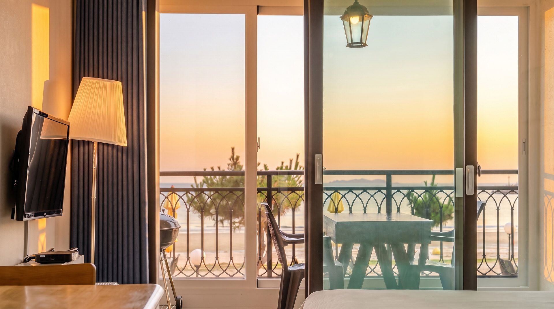 Una habitación con balcón, televisión, lámpara y vista al mar.
