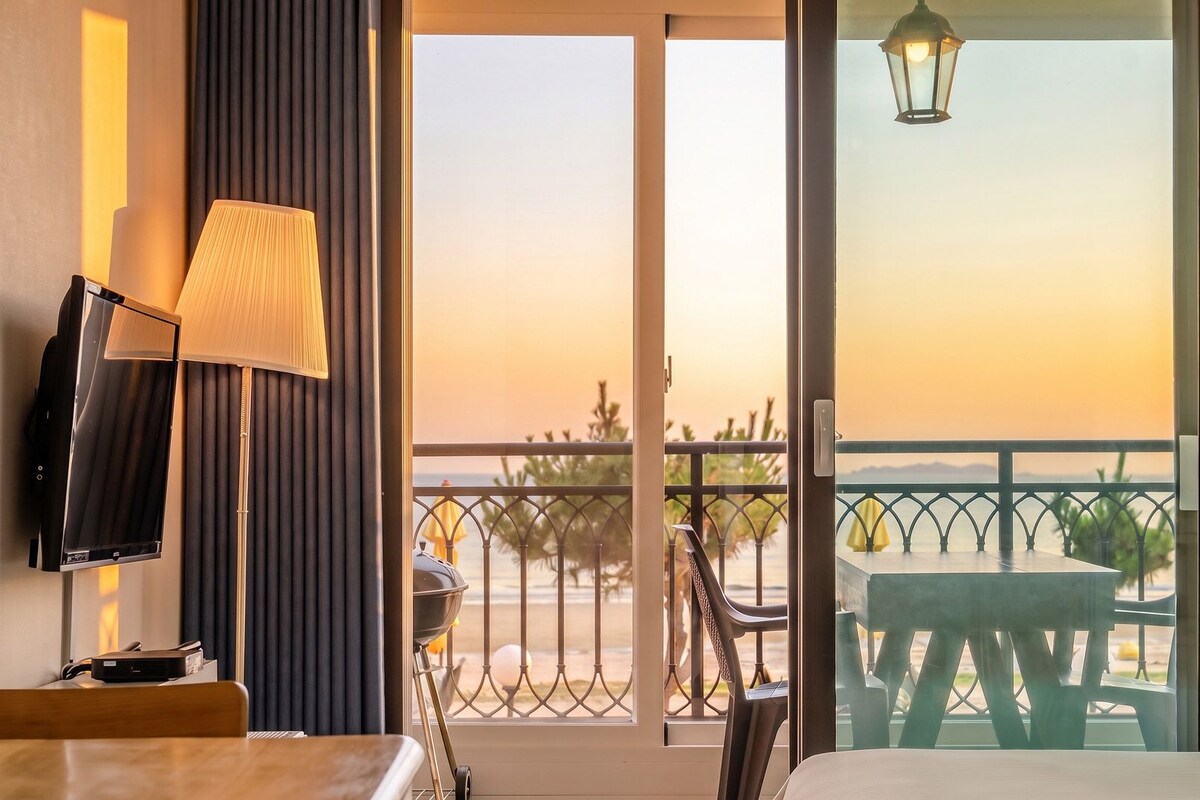 A room with a balcony, a TV, a lamp, and a view of the sea.