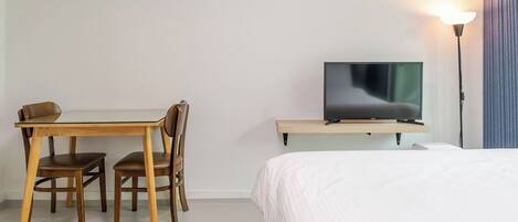 A hotel room with a bed, a TV on a stand, a desk with chairs, and a lamp.