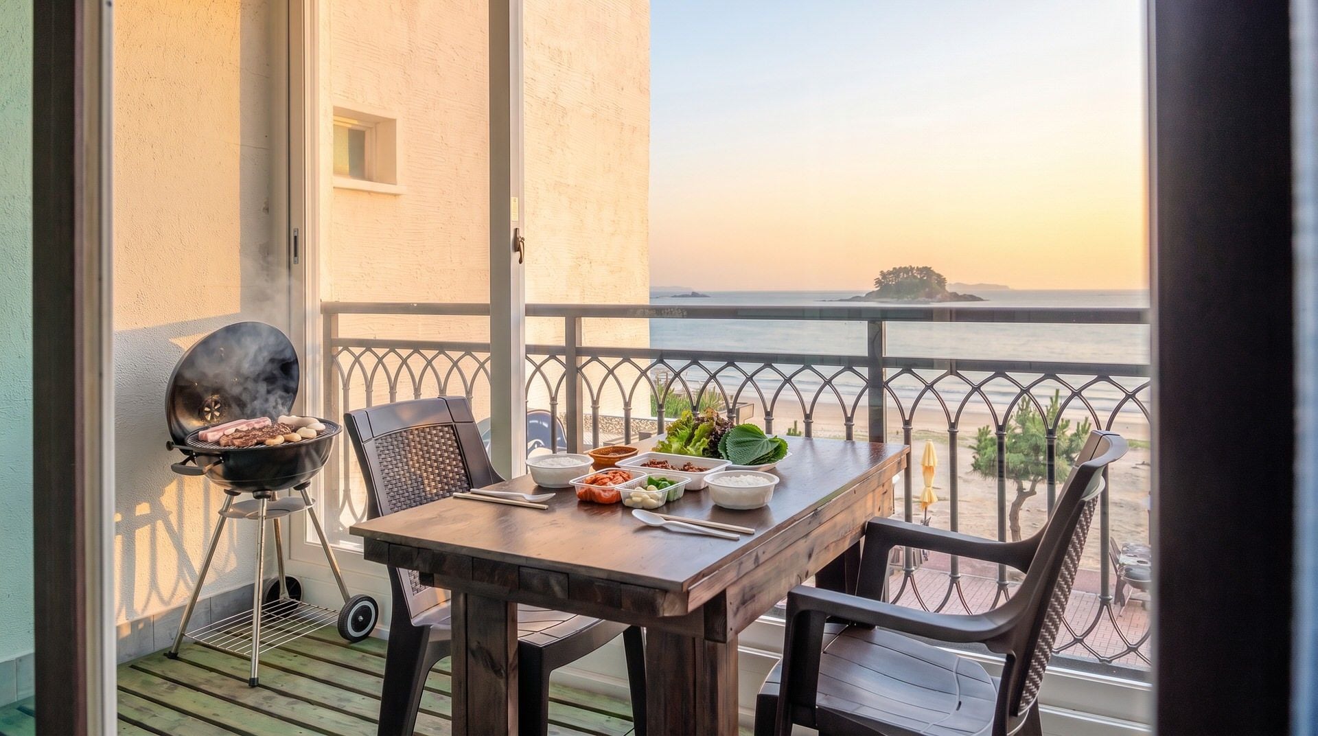 Ein Balkon mit Tisch, der für eine Mahlzeit gedeckt ist, einem Grill und Blick auf das Meer.