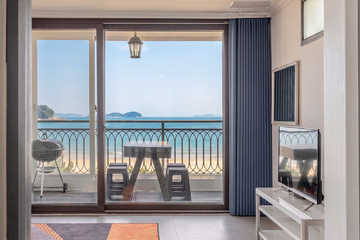A balcony with a view of the sea, a grill, and a table with chairs.
