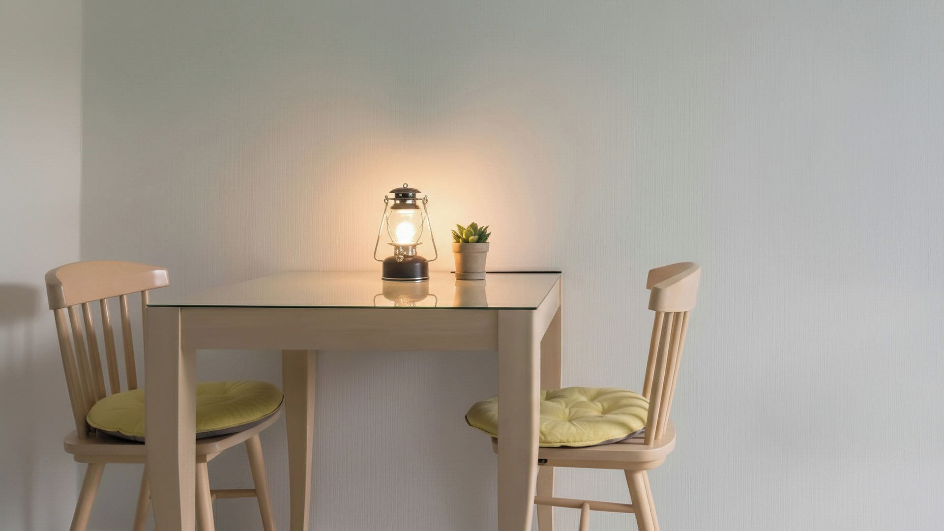 A table with two chairs, a table lamp, and a small potted plant.