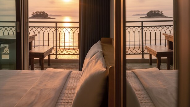 A hotel room with a bed, two wooden chairs, and a view of the sunset over the water. - The Seaside Taean (Taean)