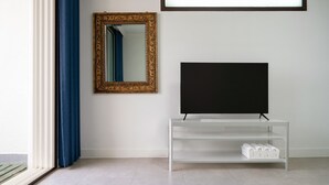 A modern living room with a large flat-screen TV on a white stand, a decorative gold-framed mirror, and a blue curtain. - The Seaside Taean (Taean)