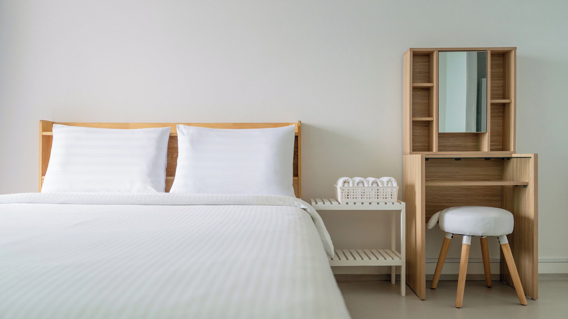 A hotel room with a bed, a wooden nightstand, a white chair, and a wooden wardrobe with a mirror.