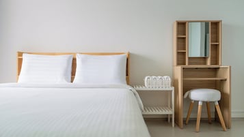 Quarto de hotel com uma cama, uma mesinha de cabeceira de madeira, uma cadeira branca e um guarda-roupa de madeira com espelho.