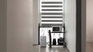 A hallway with a white wall, a window with horizontal blinds, a microwave on a shelf, and a thermostat.