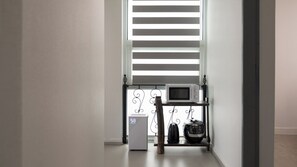 A hallway with a white wall, a window with horizontal blinds, a microwave on a shelf, and a thermostat. - The Seaside Taean (Taean)