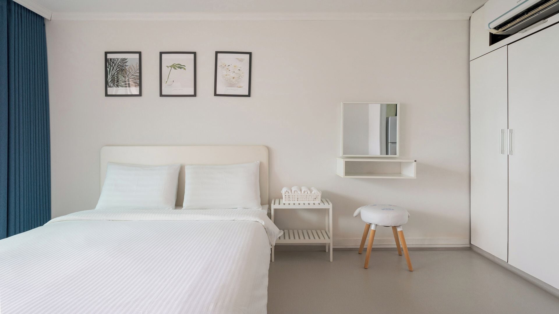 A bedroom with a bed, a bedside table with towels, a small stool, a mirror, and a wardrobe.
