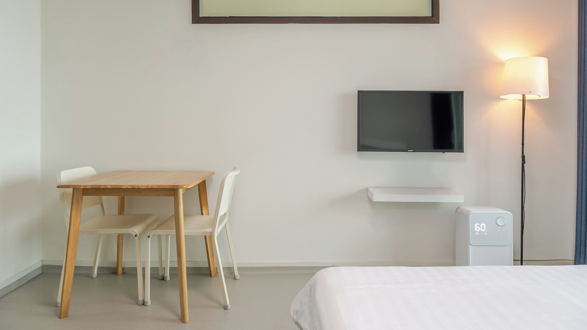 A hotel room with a bed, a desk with chairs, a television, a lamp, and a thermostat.