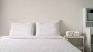 A bed with white bedding, a white nightstand with a basket of towels, and a white wall. - The Seaside Taean (Taean)
