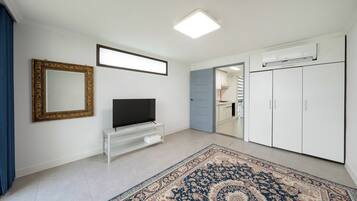 A room with a television on a stand, a large mirror, a wardrobe, and a patterned rug.