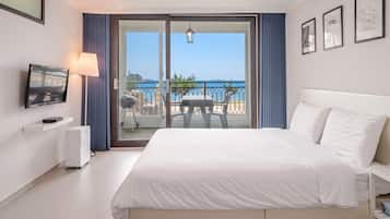 A hotel room with a bed, a television, a grill, and a balcony with a view of the sea.