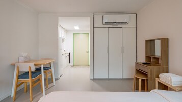 A compact hotel room with a bed, a desk with a chair, a wardrobe, and a small seating area with a table and chairs.