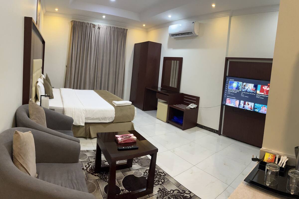 A hotel room with a bed, a sofa, a TV, a desk, and a wardrobe.