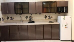 A kitchen with dark cabinets, a microwave, and a refrigerator. - Danat Al Sharq Serviced Apartments (Al Khobar)