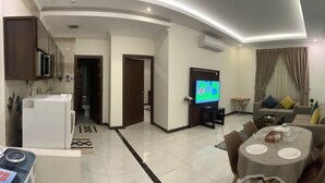 A modern living room with a dining area, a kitchen, and a TV. - Danat Al Sharq Serviced Apartments (Al Khobar)