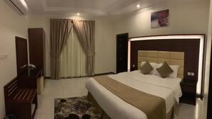 A hotel room with a bed, bedside tables, a desk, a mirror, a window with curtains, and a picture on the wall. - Danat Al Sharq Serviced Apartments (Al Khobar)