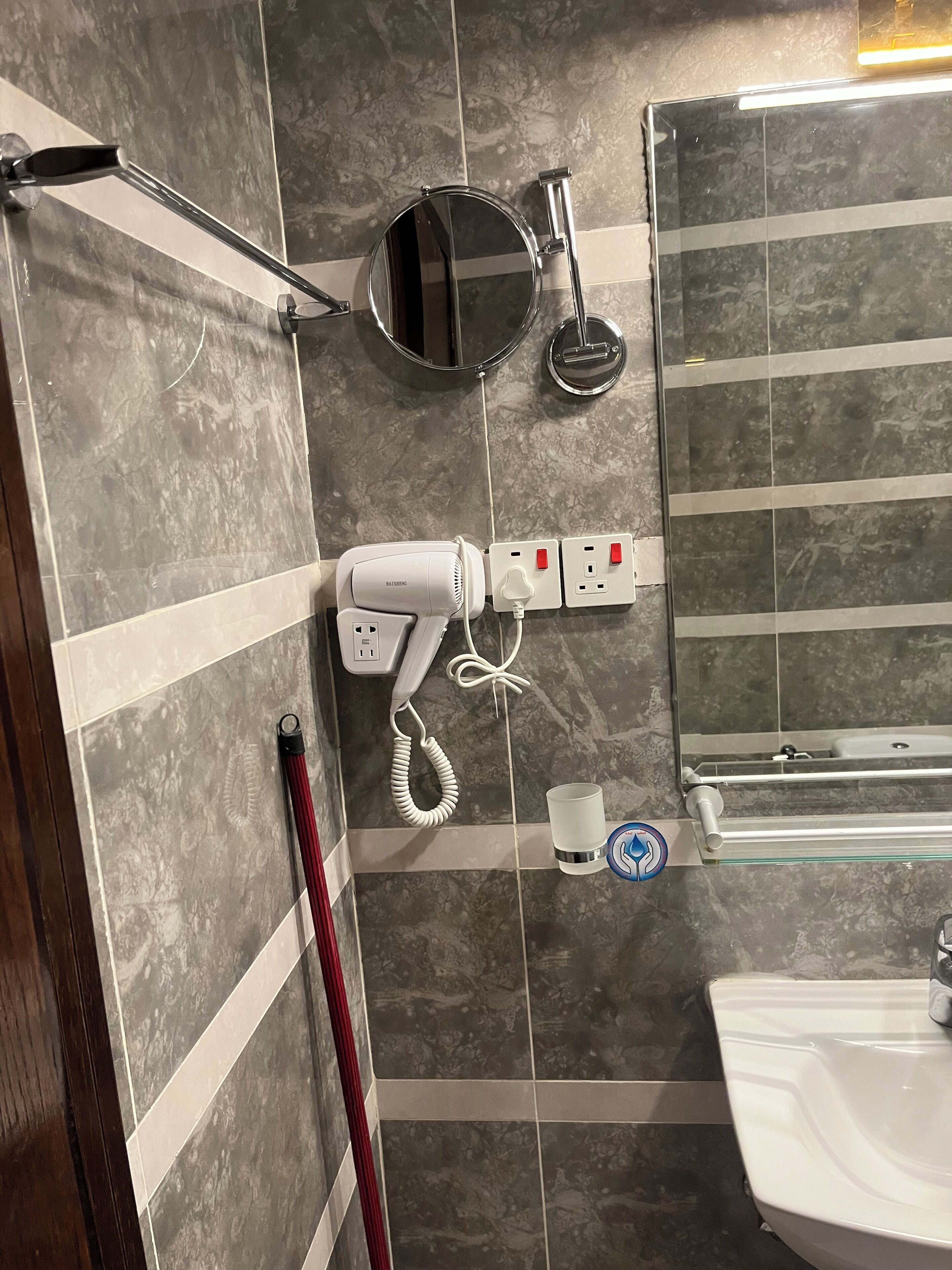 A bathroom with a hairdryer, a mirror, a towel rack, a glass shower enclosure, and a sink.