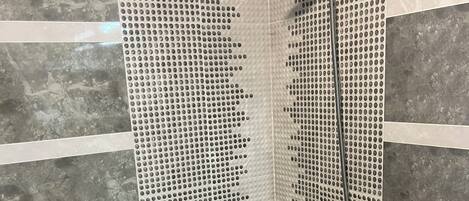 A shower with a perforated wall, a handheld showerhead, and a floor drain.