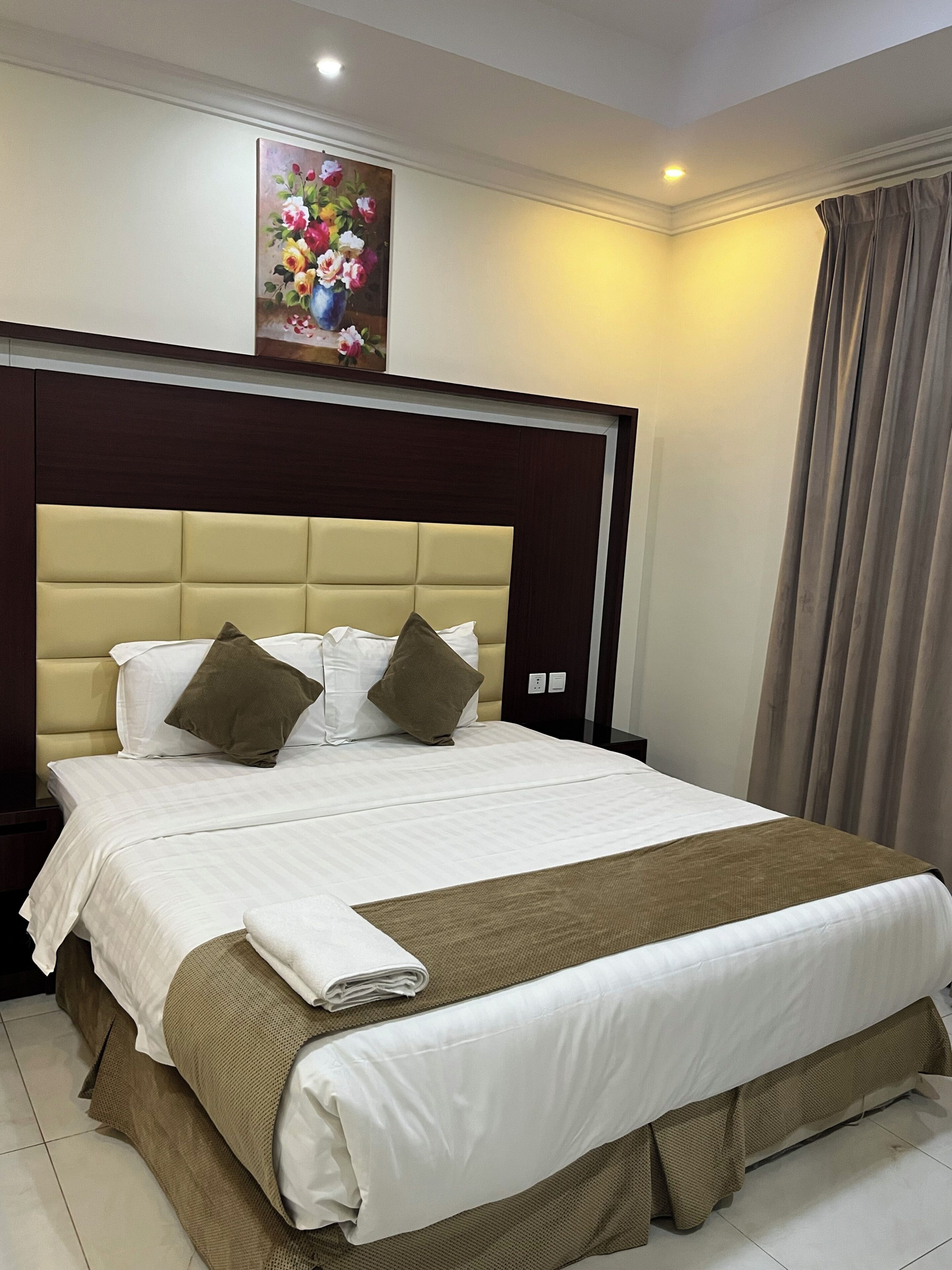 Quarto de hotel com cama grande, cabeceira, um quadro na parede e cortina.