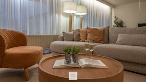 A modern living room with a sofa, armchair, and a coffee table with a book and glasses. - Boulevard Floor, top location and parking incl. (Knokke-Heist)
