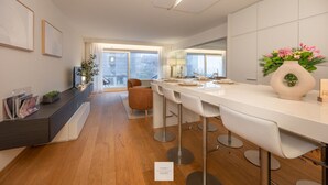 A modern kitchen with a long countertop, bar stools, and a dining table set for four. - Boulevard Floor, top location and parking incl. (Knokke-Heist)
