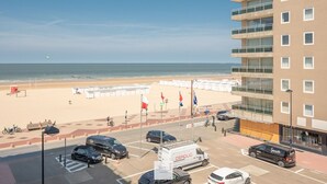 A beachside view from a high-rise building with a parking lot, beach umbrellas, and flags. - Boulevard Floor, top location and parking incl. (Knokke-Heist)