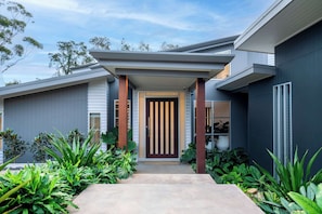 A modern house with a dark exterior, a front porch, and a door with vertical stripes. - Stonewood by Coast Hosting (North Avoca)