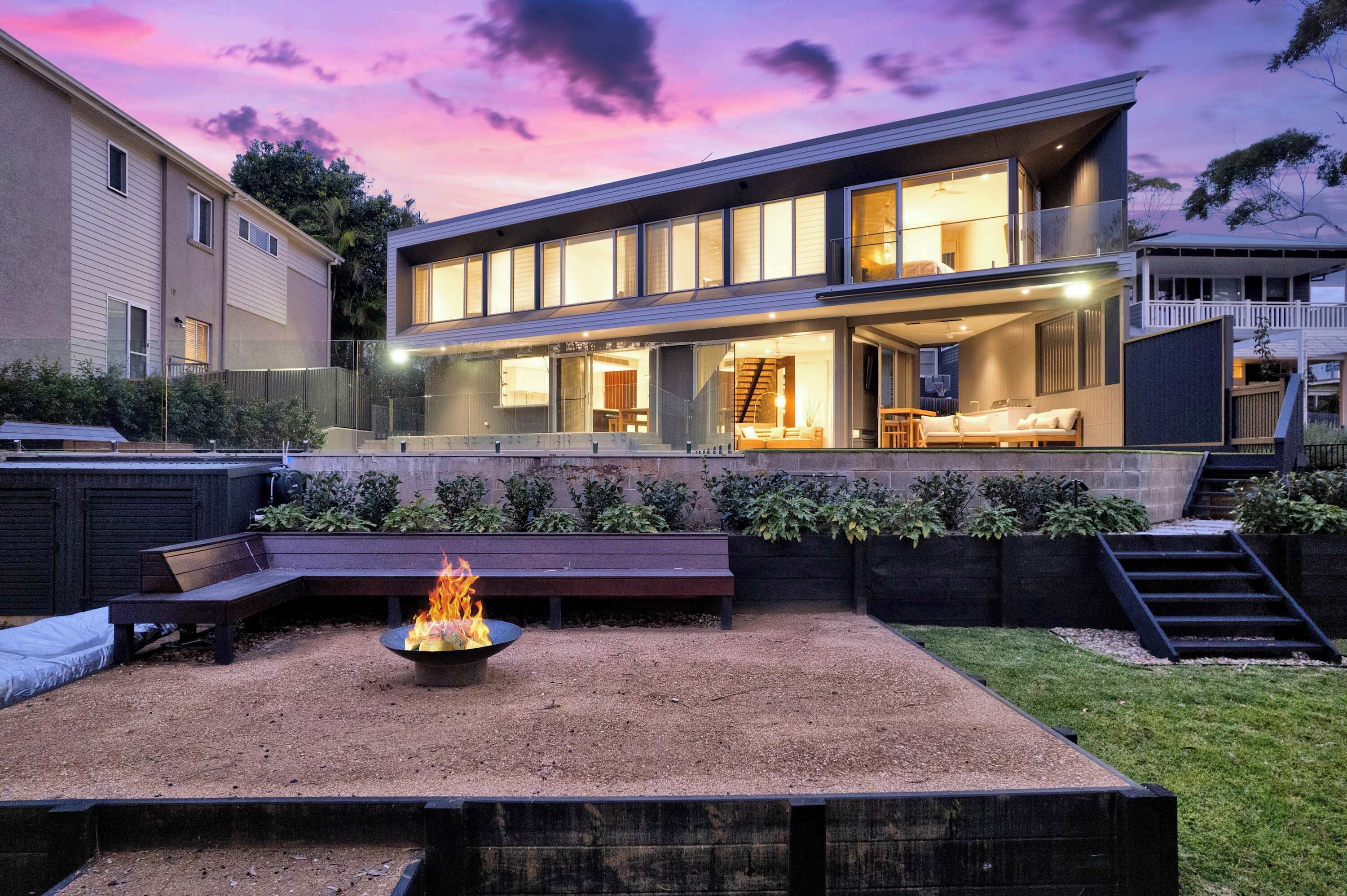 A modern house with a spacious backyard, a fire pit, and a staircase leading to a deck.