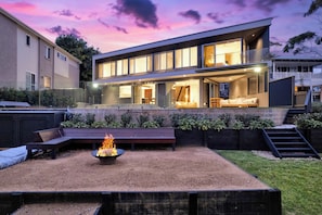 A modern house with a spacious backyard, a fire pit, and a staircase leading to a deck. - Stonewood by Coast Hosting (North Avoca)