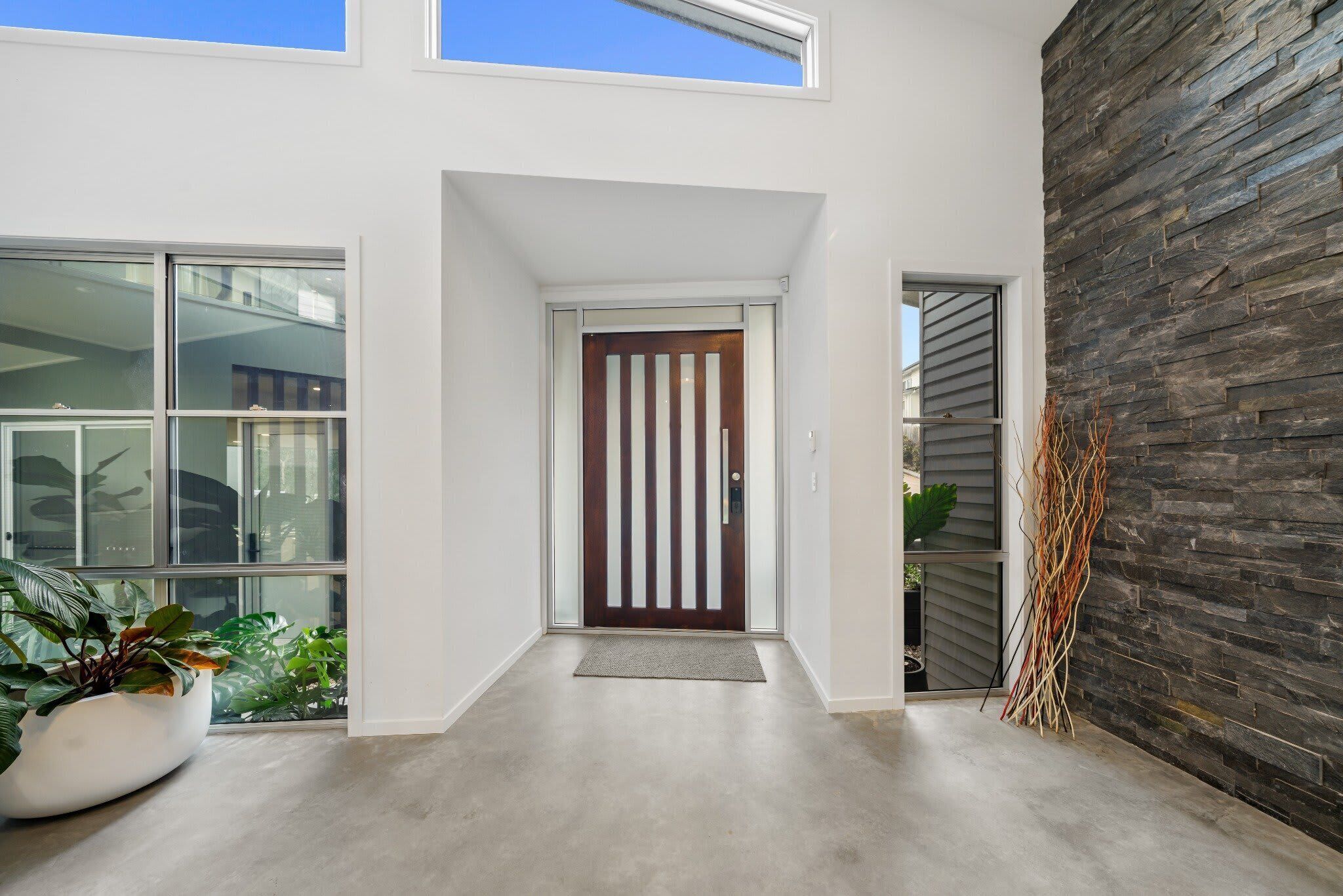 Une entrée moderne avec une porte en bois, de grandes fenêtres et un mur en pierre.