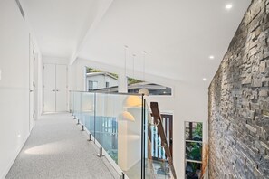 Un interior moderno con barandilla de cristal, pared de piedra y escalera que conduce a un nivel superior.