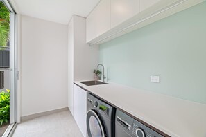 A compact kitchen with a washing machine, a sink, and a small potted plant. - Stonewood by Coast Hosting (North Avoca)