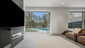 En moderne stue med pejs, sofa og udsigt til en swimmingpool.