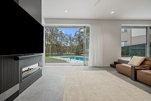 Ein modernes Wohnzimmer mit Kamin, einer Couch und Blick auf einen Swimmingpool.
