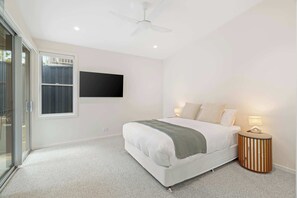 Ein Schlafzimmer mit Bett, Nachttisch mit Lampe, Deckenventilator und einem an der Wand befestigten Fernseher.