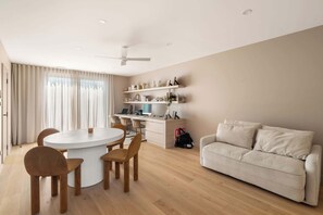 Una sala de estar moderna con una mesa redonda de comedor, sillas de madera, un sofá beige y un escritorio con estanterías.