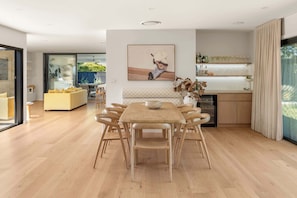 Una cocina moderna con comedor, que incluye una mesa grande de madera y sillas, una isla de cocina y un amplio ventanal con cortinas.