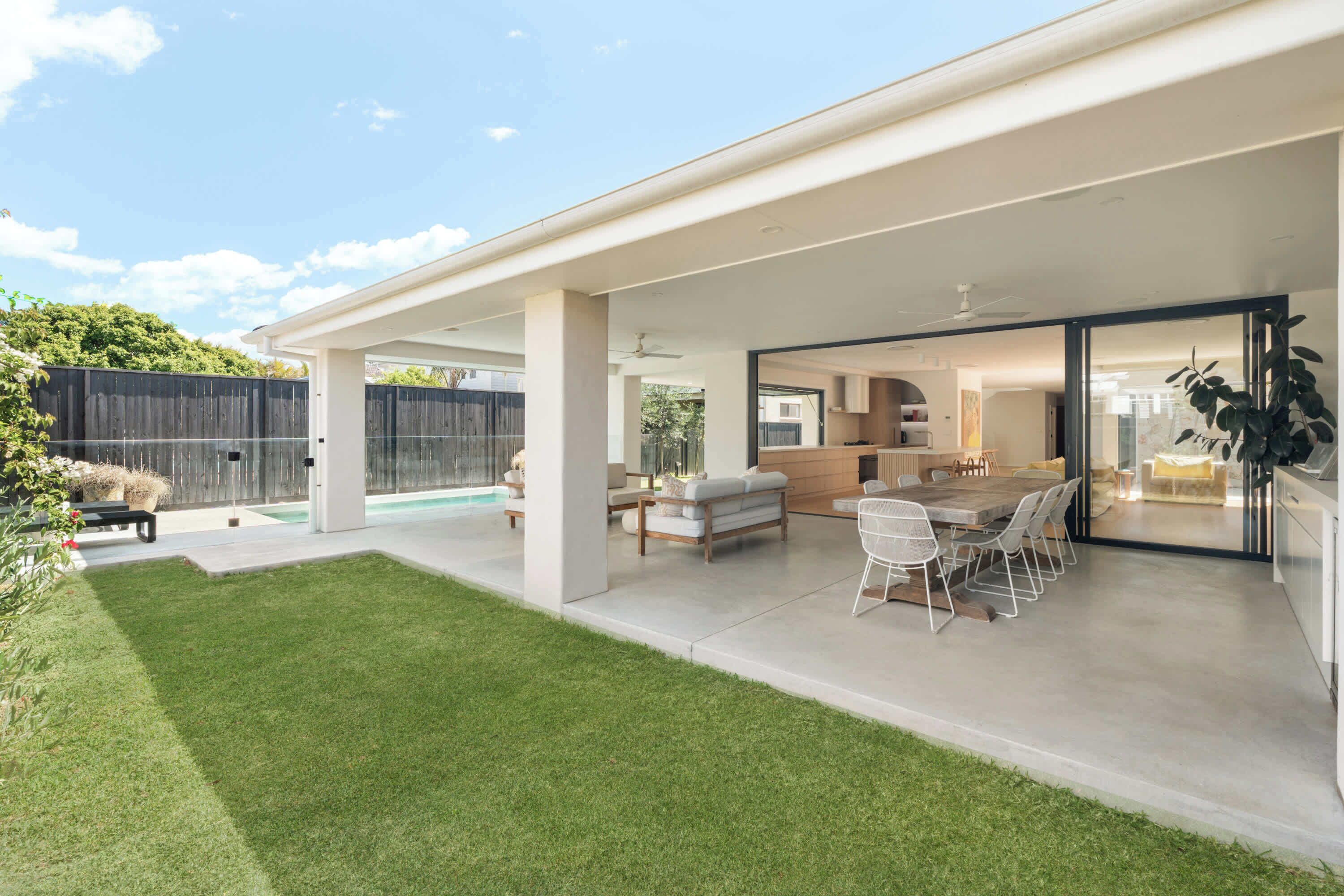 Une maison moderne dotée d’un patio couvert, d’un coin repas et d’une cuisine visible à travers des portes vitrées.
