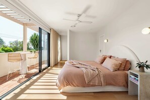 Un dormitorio moderno con una cama grande, un ventilador de techo y un balcón con zona de comedor.