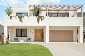 Una casa moderna de dos pisos con techo plano, un porche cubierto y un garaje.