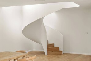 A modern interior with a spiral staircase, wooden flooring, and a dining area with chairs. - Sol House by Coast Hosting (North Avoca)