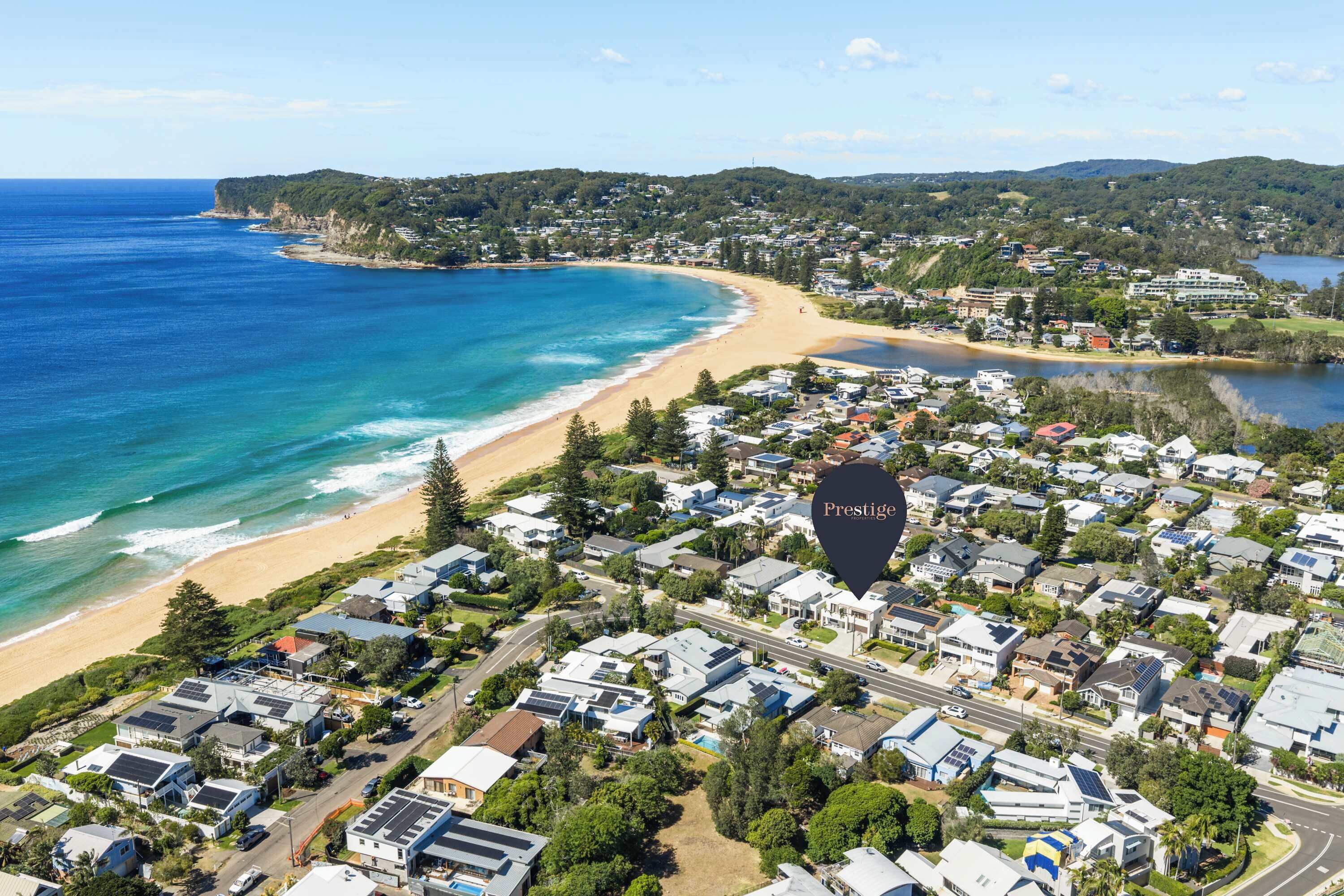 An aerial view of a coastal residential area with houses, a beach, and a large body of water.