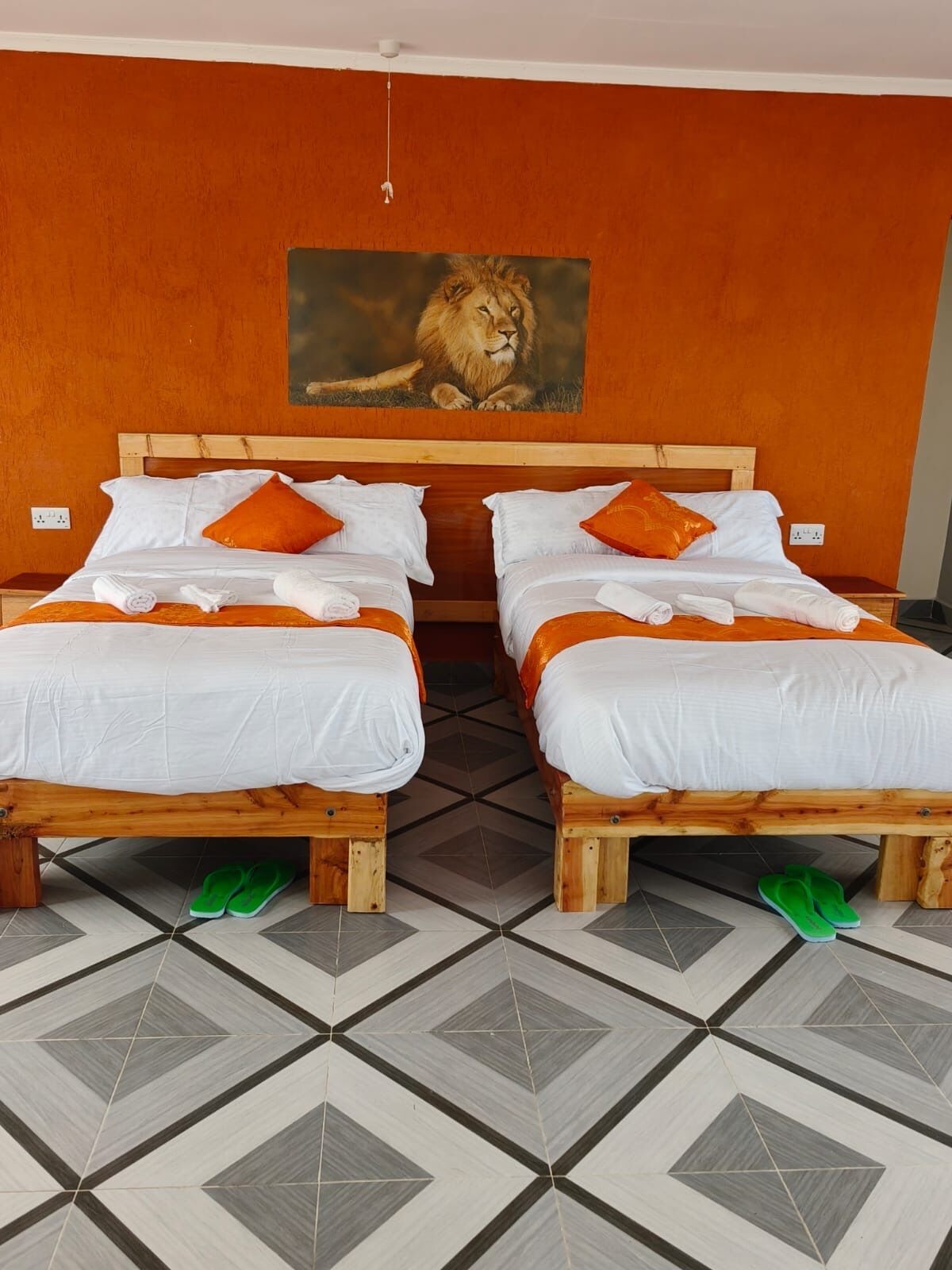 Een hotelkamer met twee houten bedden, witte beddengoed, oranje kussens en een schilderij van een leeuw aan de muur.