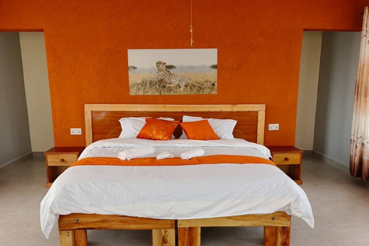 Un dormitorio con cama de madera, ropa de cama blanca, almohadas anaranjadas y un cuadro de un guepardo en la pared.