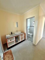 Un baño moderno con lavamanos de mármol, un espejo y un inodoro visible a través de una puerta de cristal.