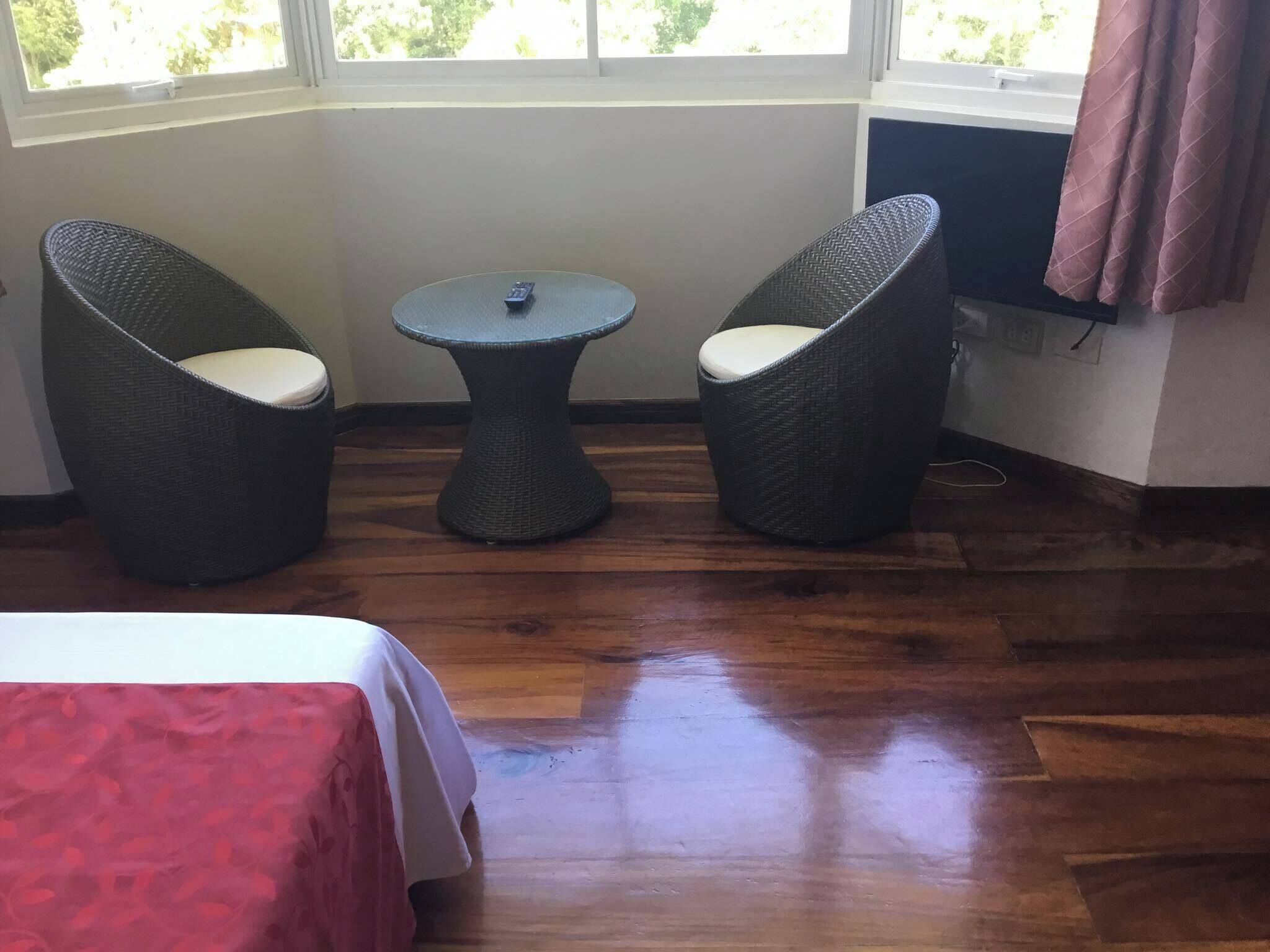 Une pièce comprenant un lit, deux fauteuils en osier, une petite table et une fenêtre avec des rideaux.