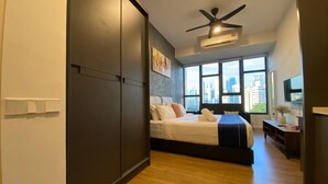 Un dormitorio moderno con cama, ventilador de techo, ventana grande con vista a la ciudad y televisor sobre un mueble bajo.