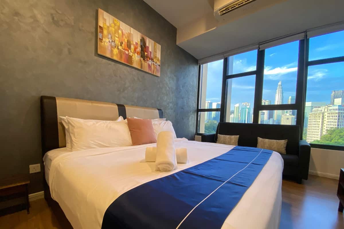 Une chambre d’hôtel avec un grand lit, une vue sur la ville par les fenêtres et un tableau accroché au mur.